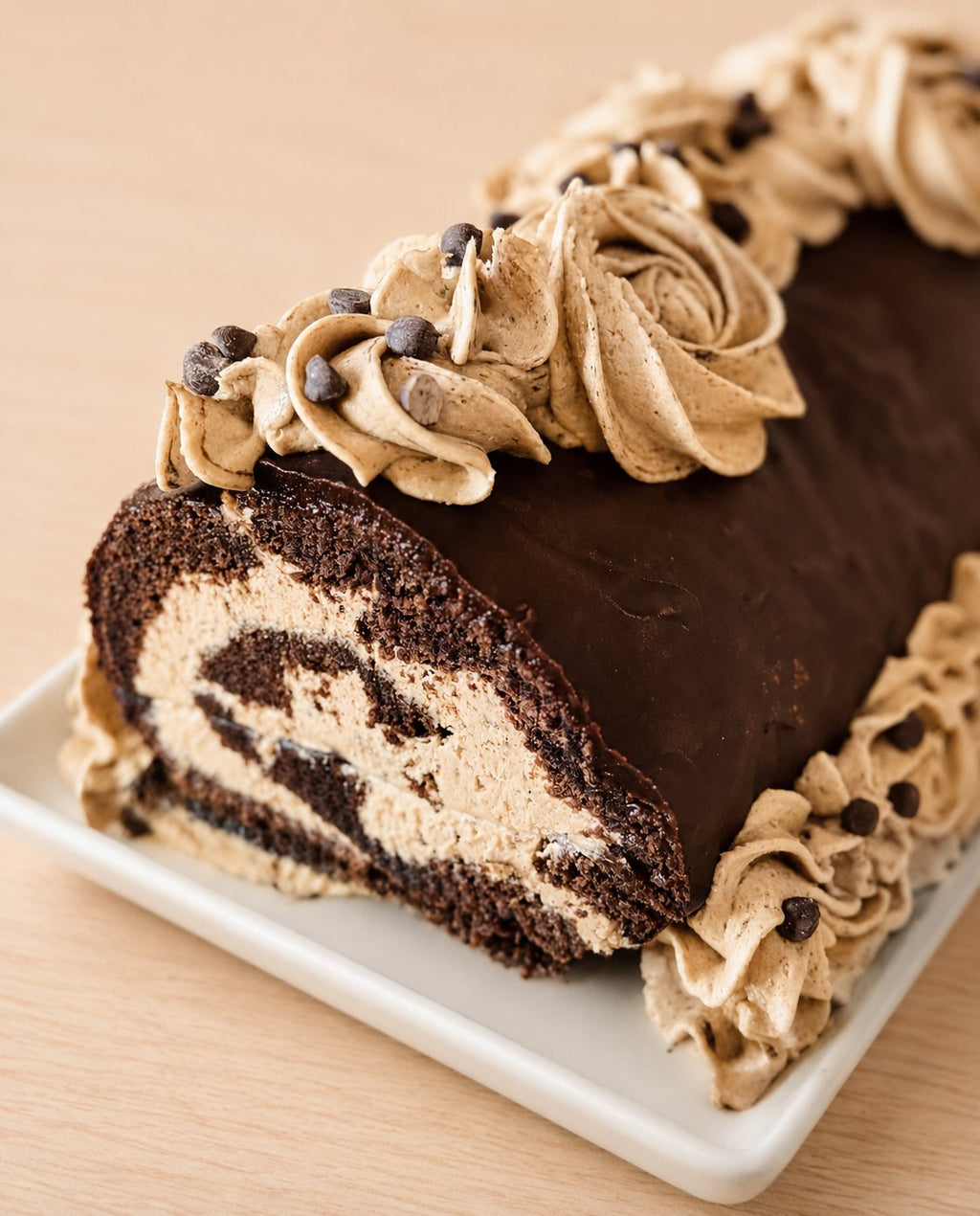 Gluten-free chocolate espresso Swiss roll topped with chocolate ganache and piped espresso buttercream rosettes with mini chocolate chips